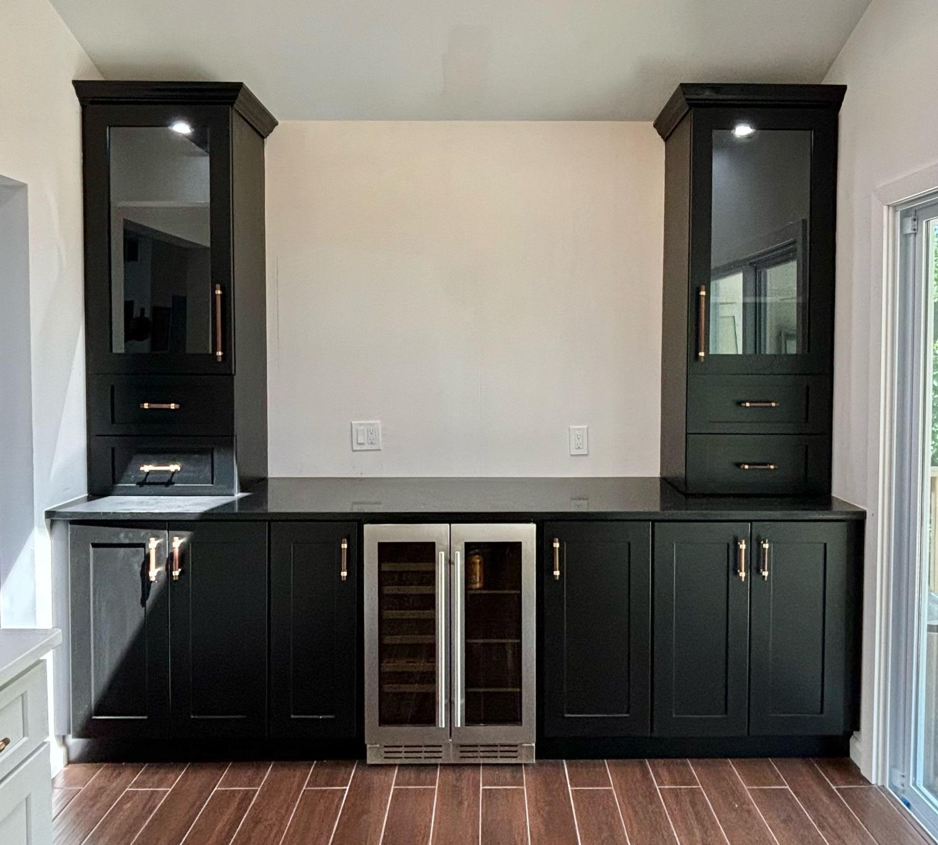 Black built-in bar with upper glass-door cabinets, lower cabinets, wine fridge, and black countertop.
