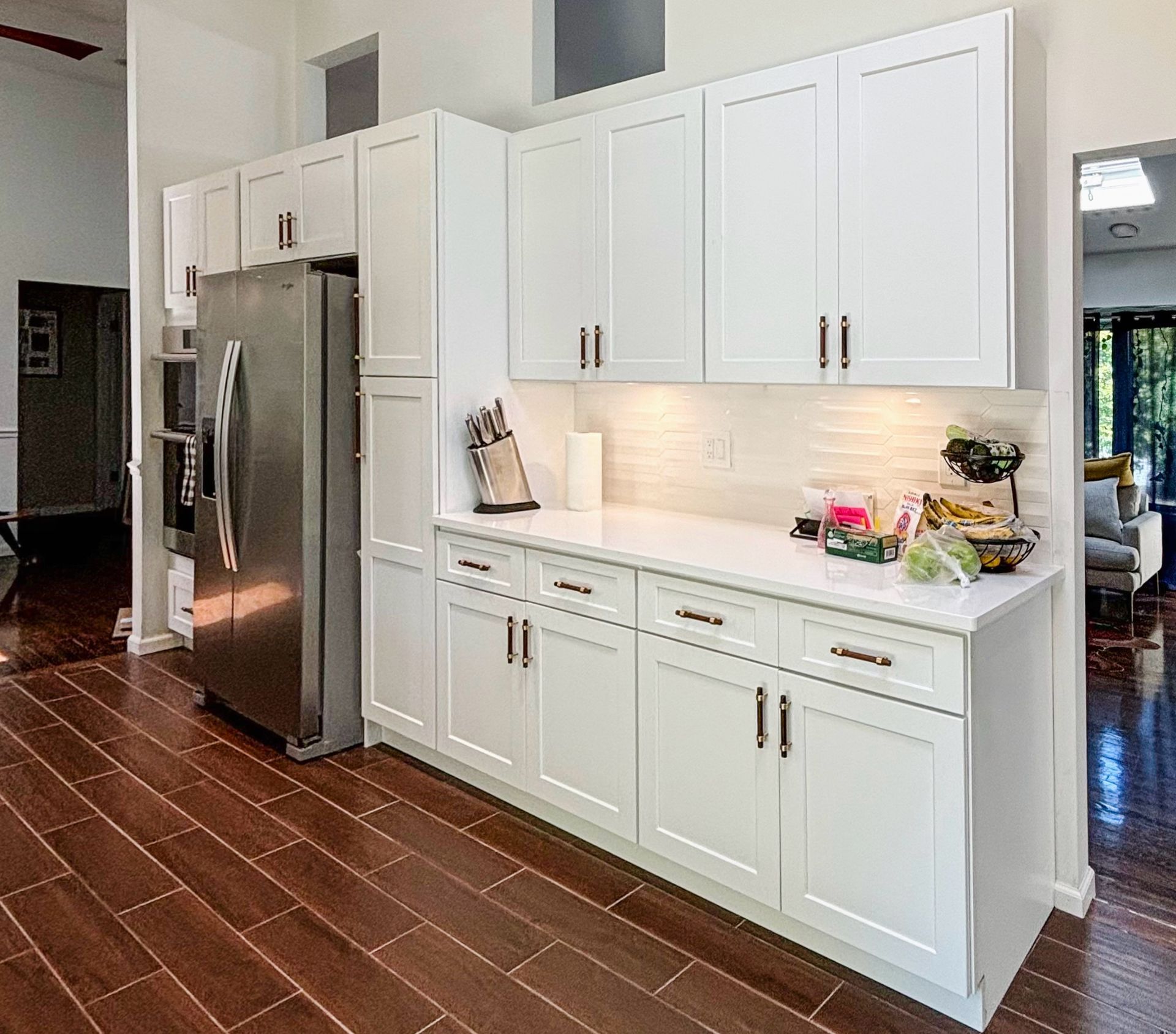 White kitchen cabinets with stainless steel refrigerator on dark wood floor.