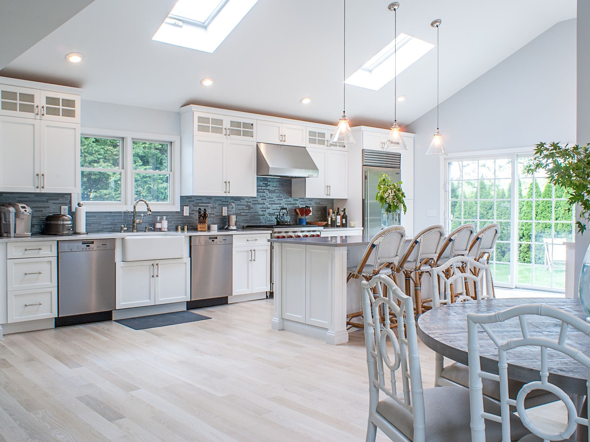 White kitchen with light wood floors, stainless steel appliances, island with seating, and skylights.