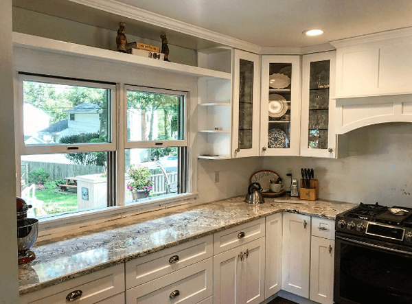 White kitchen with granite countertops, cabinets, windows, and a stove.