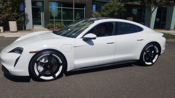 A white porsche taycan is parked in front of a building.