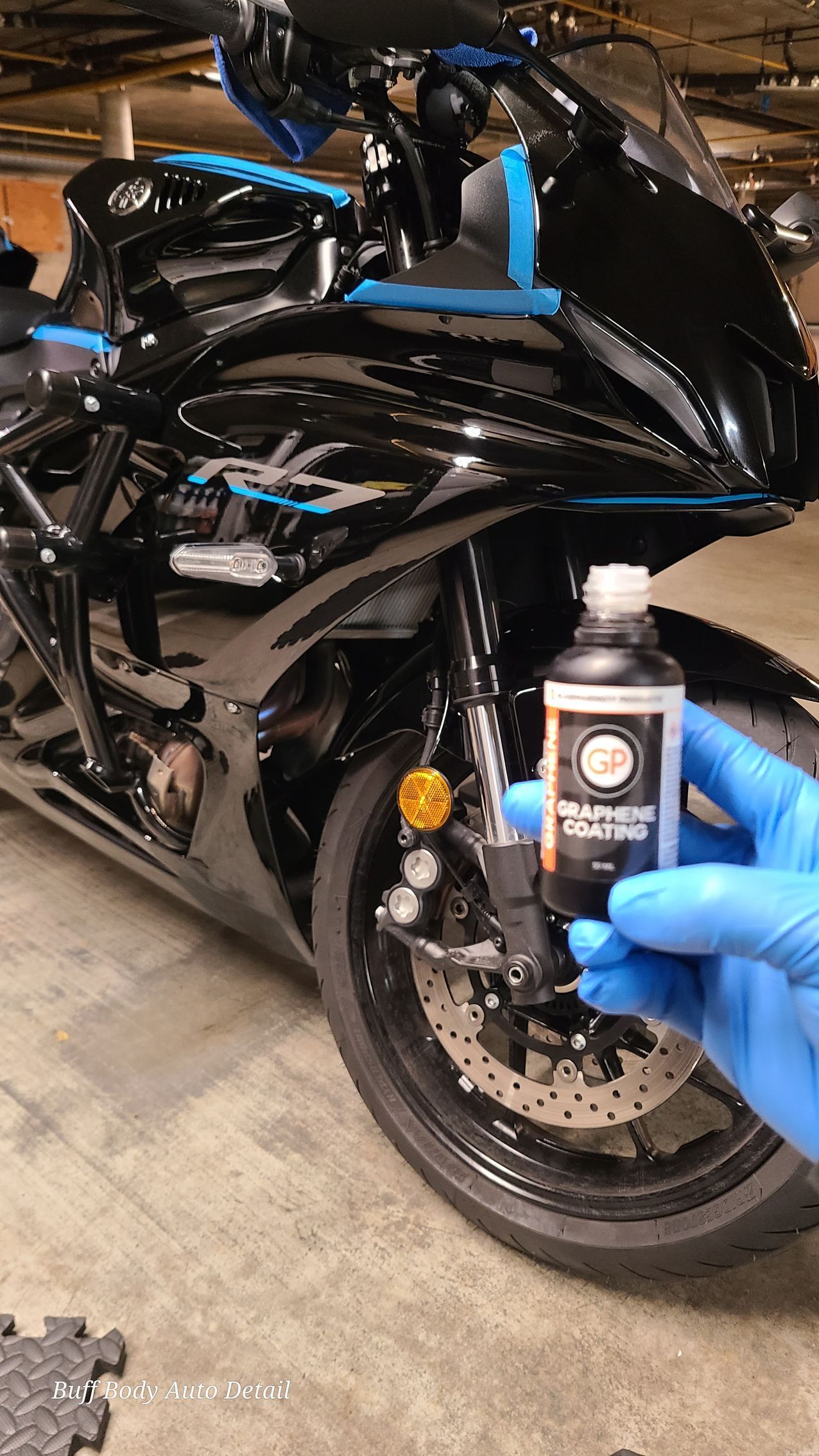 A person is holding a bottle of oil in front of a motorcycle.