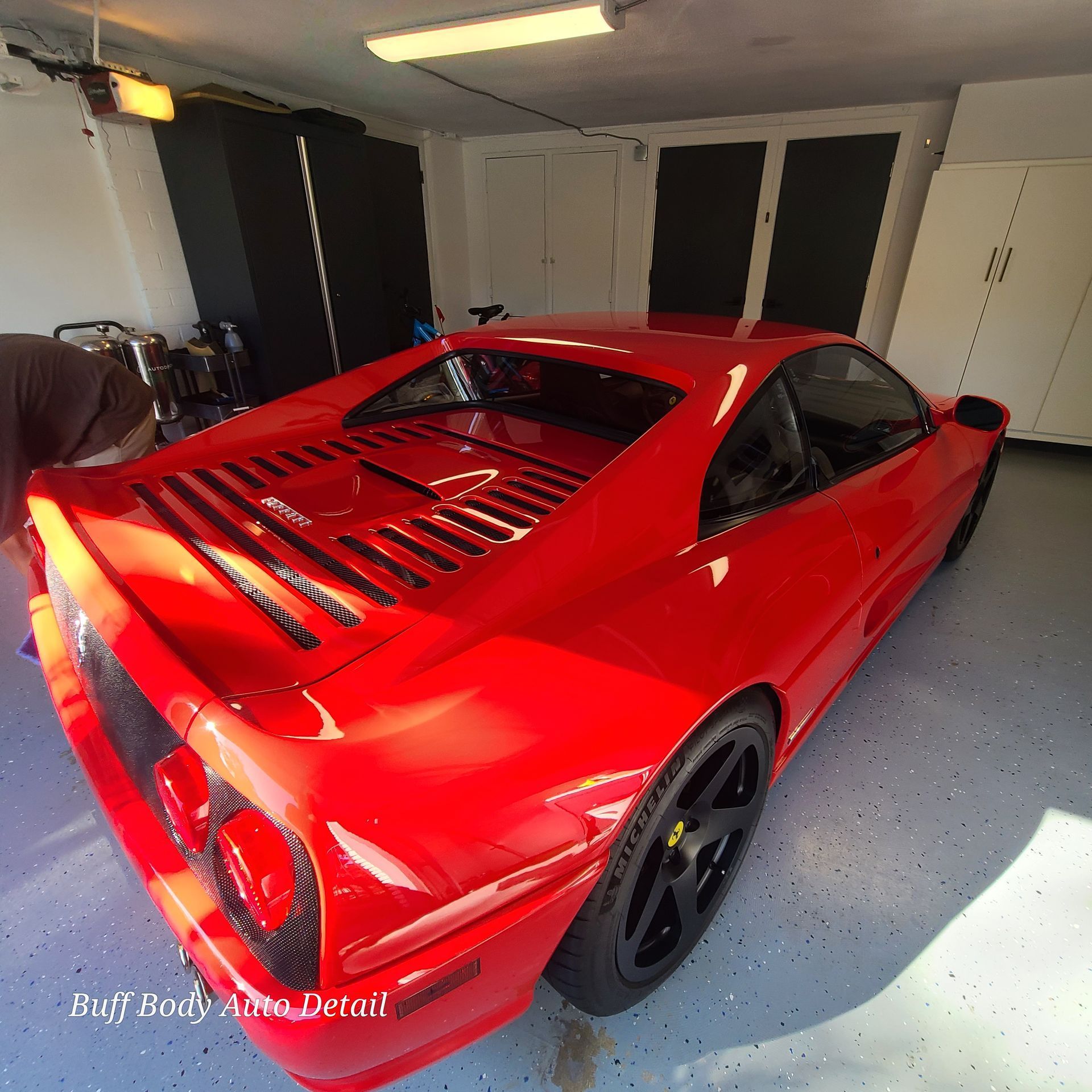 A red sports car is parked in a garage by buff body auto detail