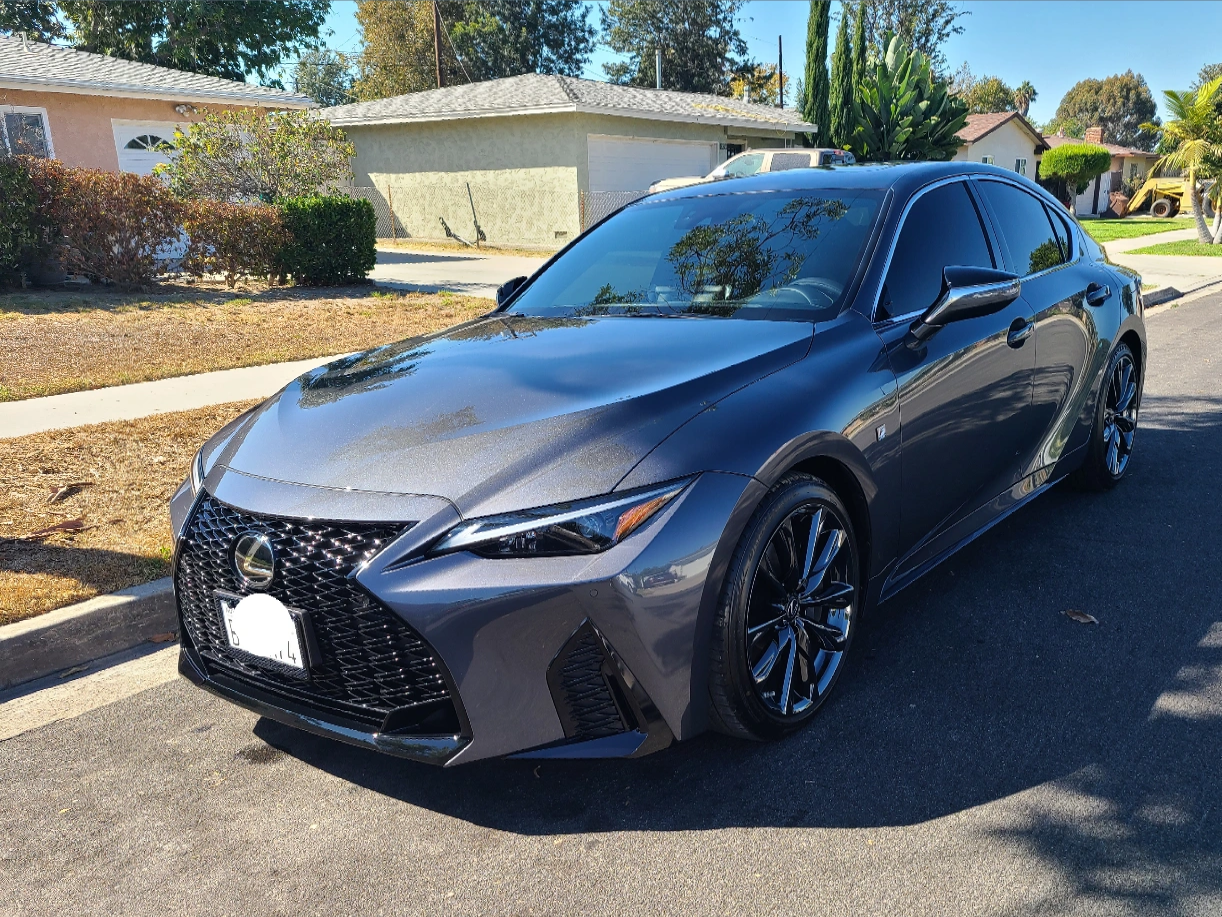 A gray lexus is parked on the side of the road in front of a house.