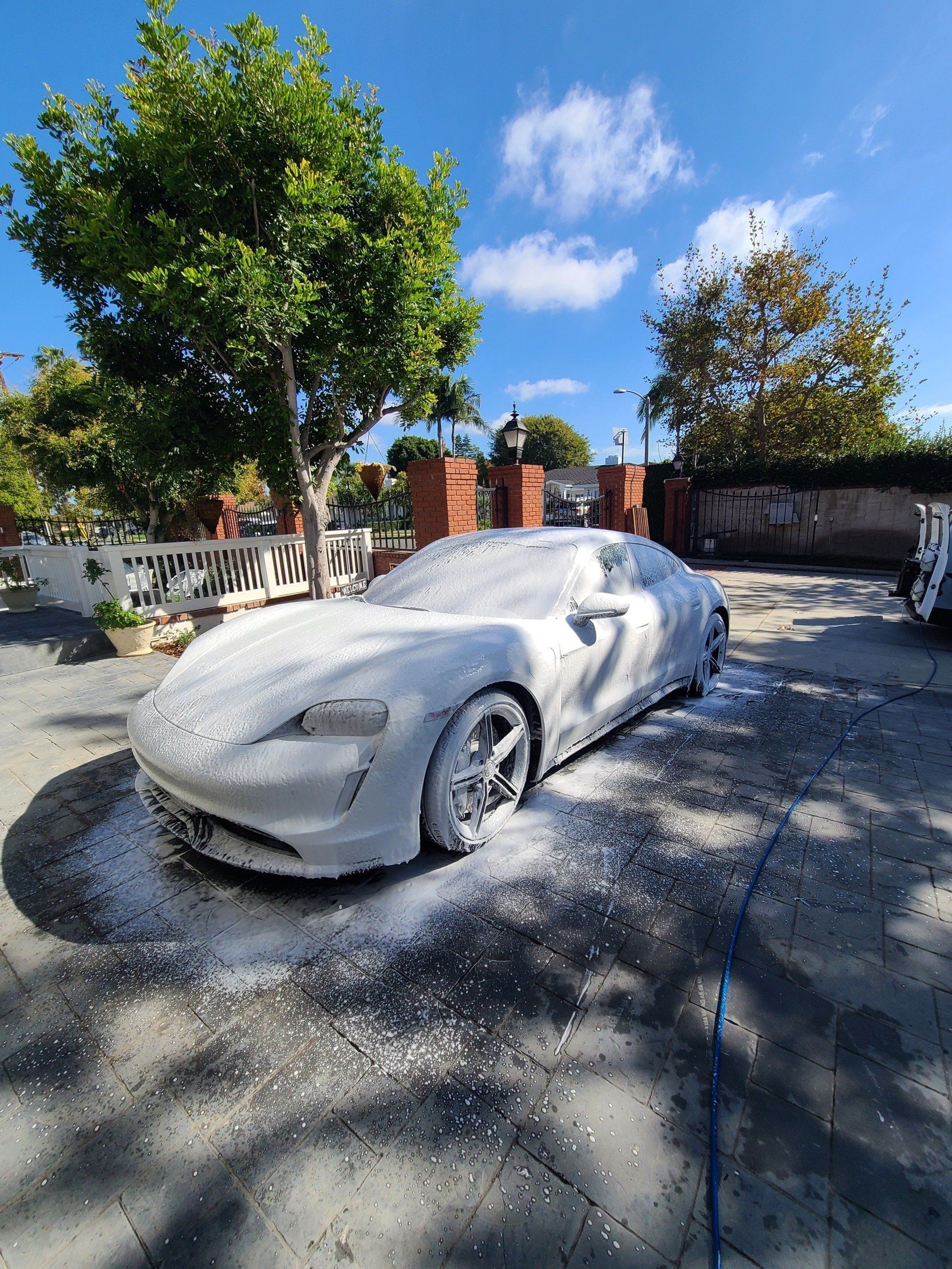 A white sports car is covered in foam in a driveway.
