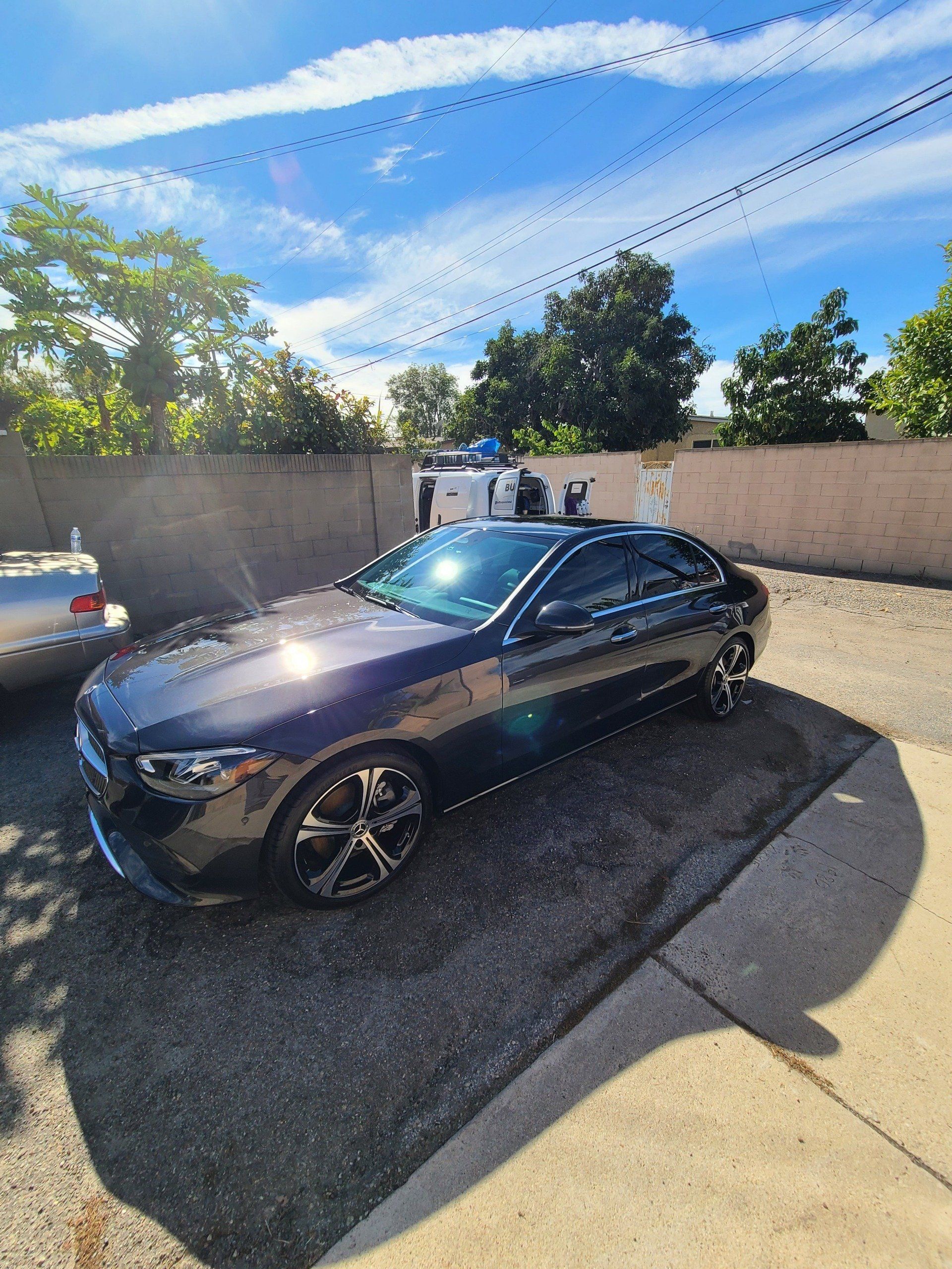 A black car is parked in a driveway next to a fence.