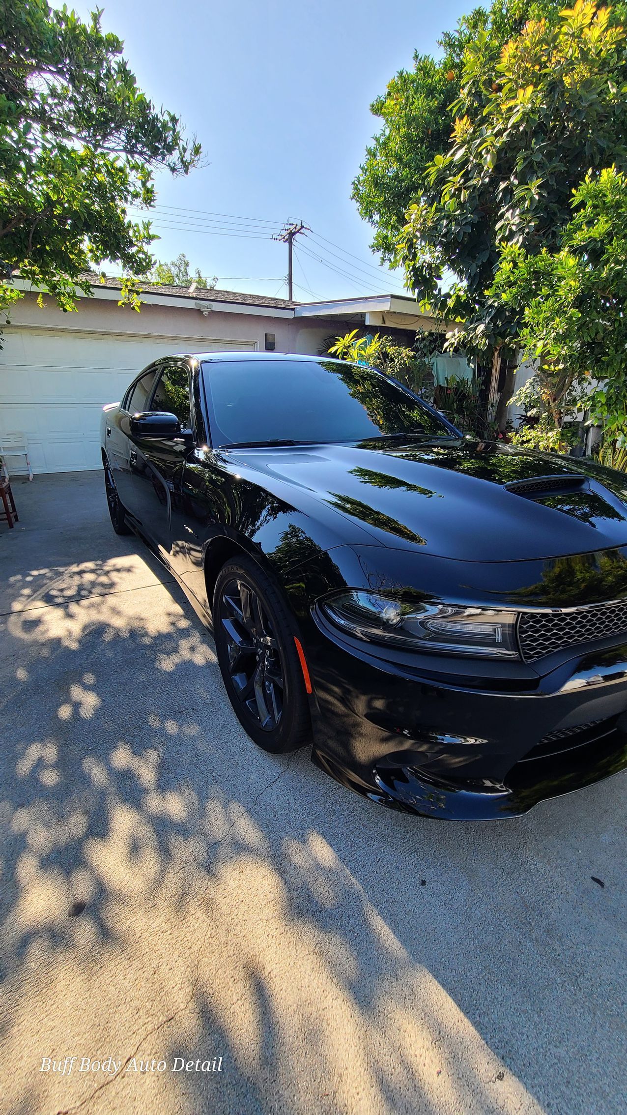 A black dodge charger is parked in a driveway next to a garage.