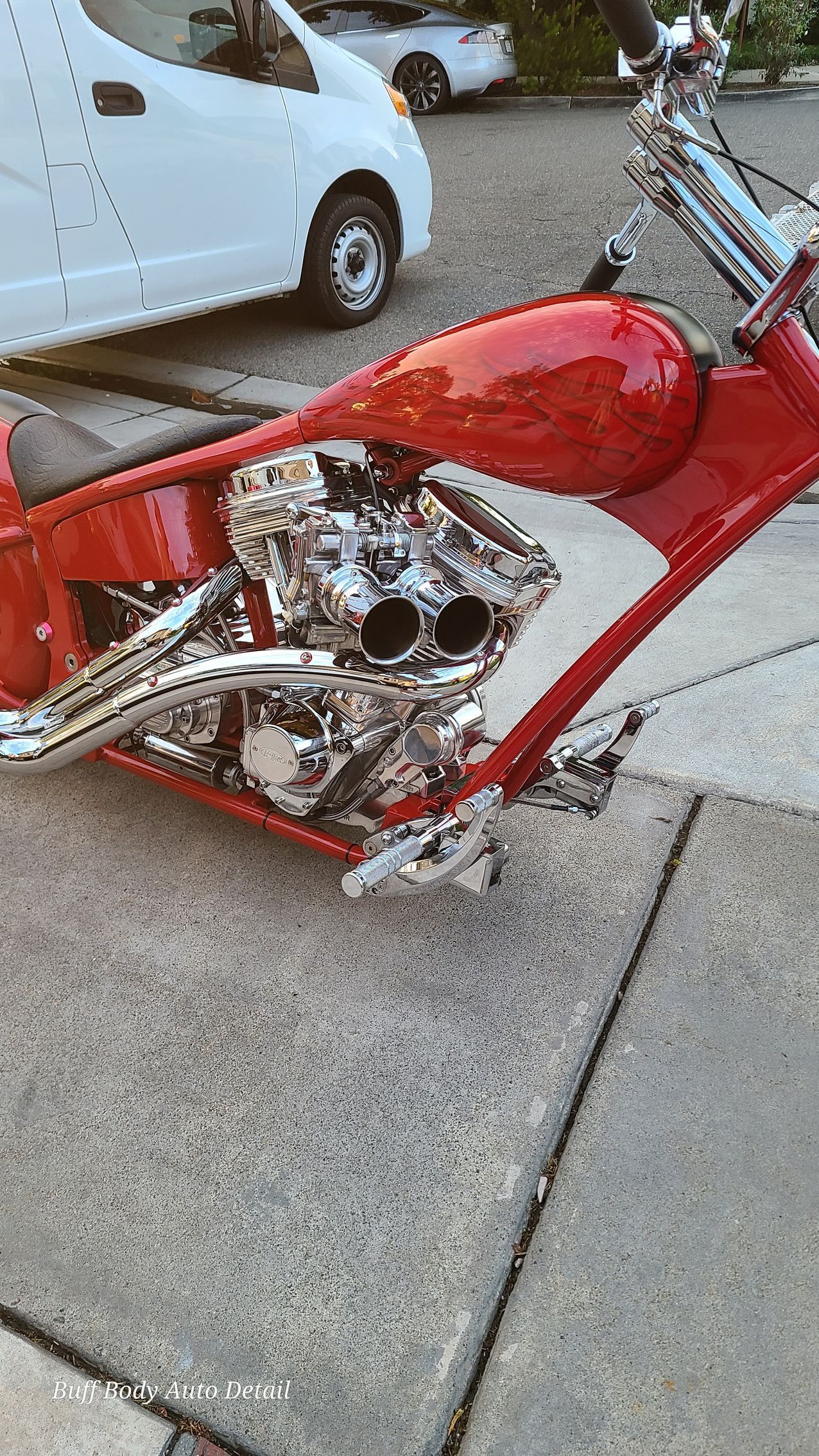 A red motorcycle is parked on the sidewalk next to a white van.