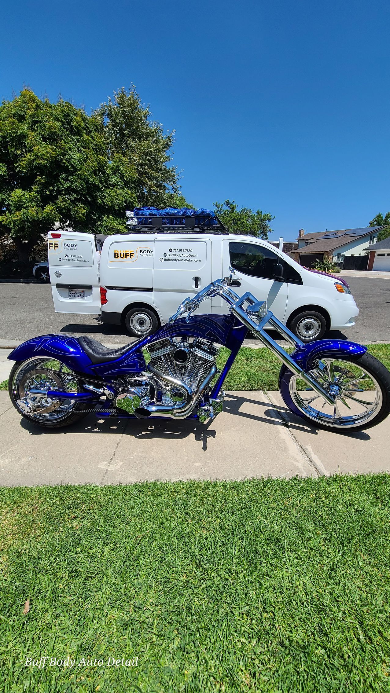 A blue chopper motorcycle is parked on the sidewalk next to a white van.