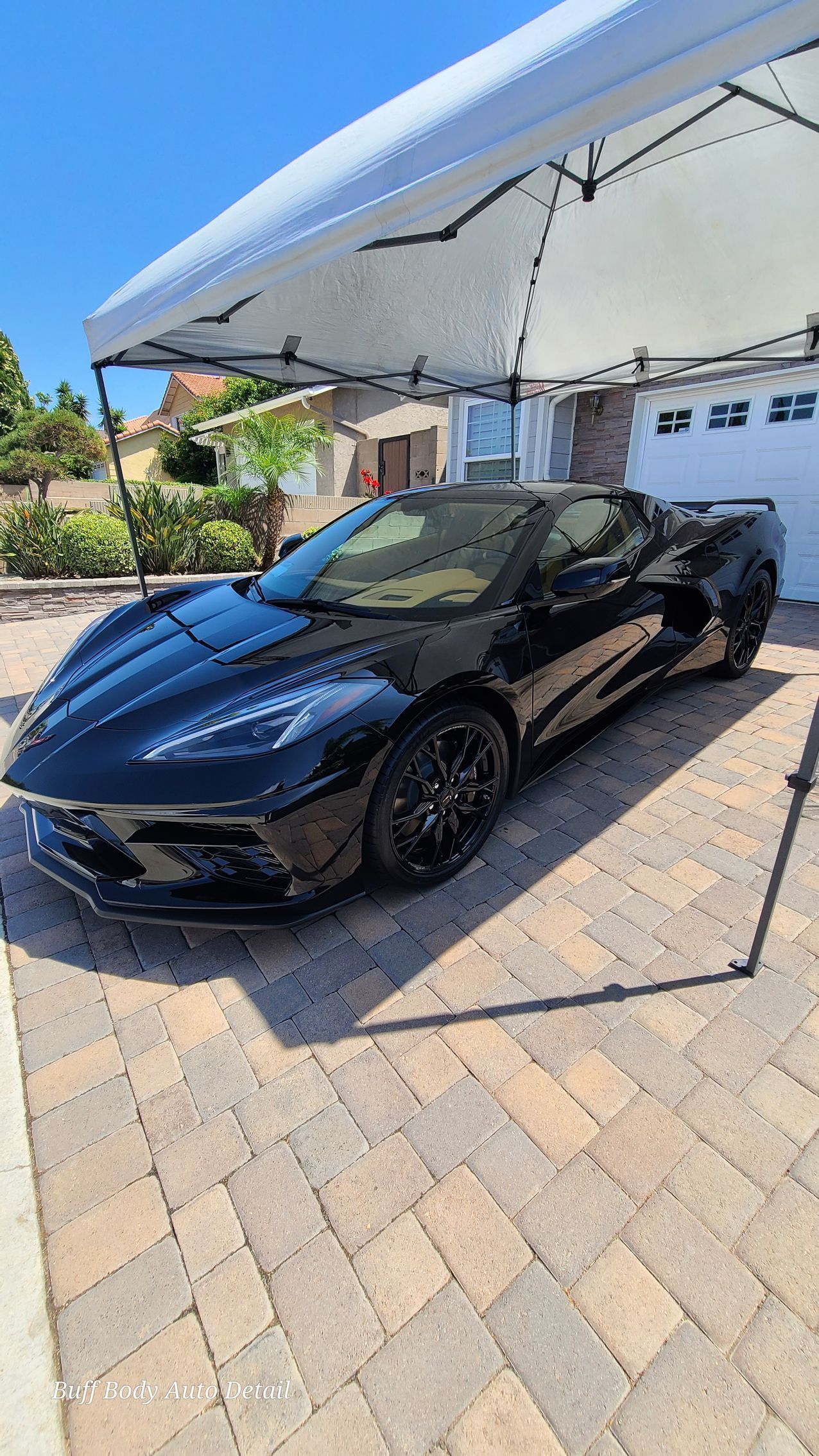 A black sports car is parked under a tent in a driveway.