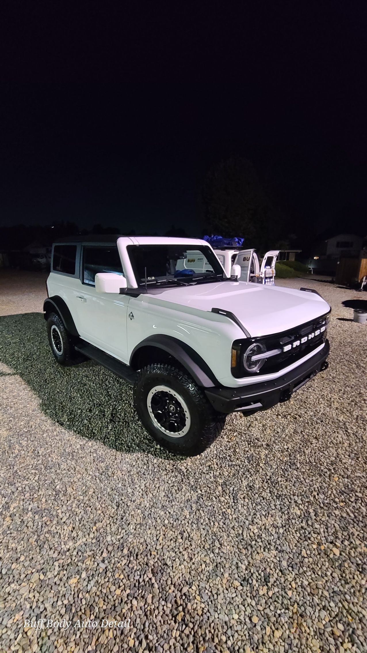 A white ford bronco is parked in a gravel lot at night.