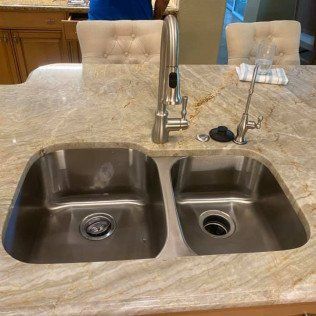 A kitchen sink with two sinks and a faucet on a granite counter top.