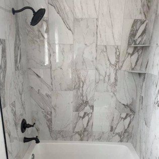 There is a bathtub in the shower with marble tiles.