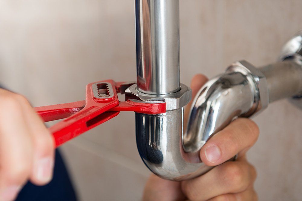 A plumber is fixing a pipe with a wrench.