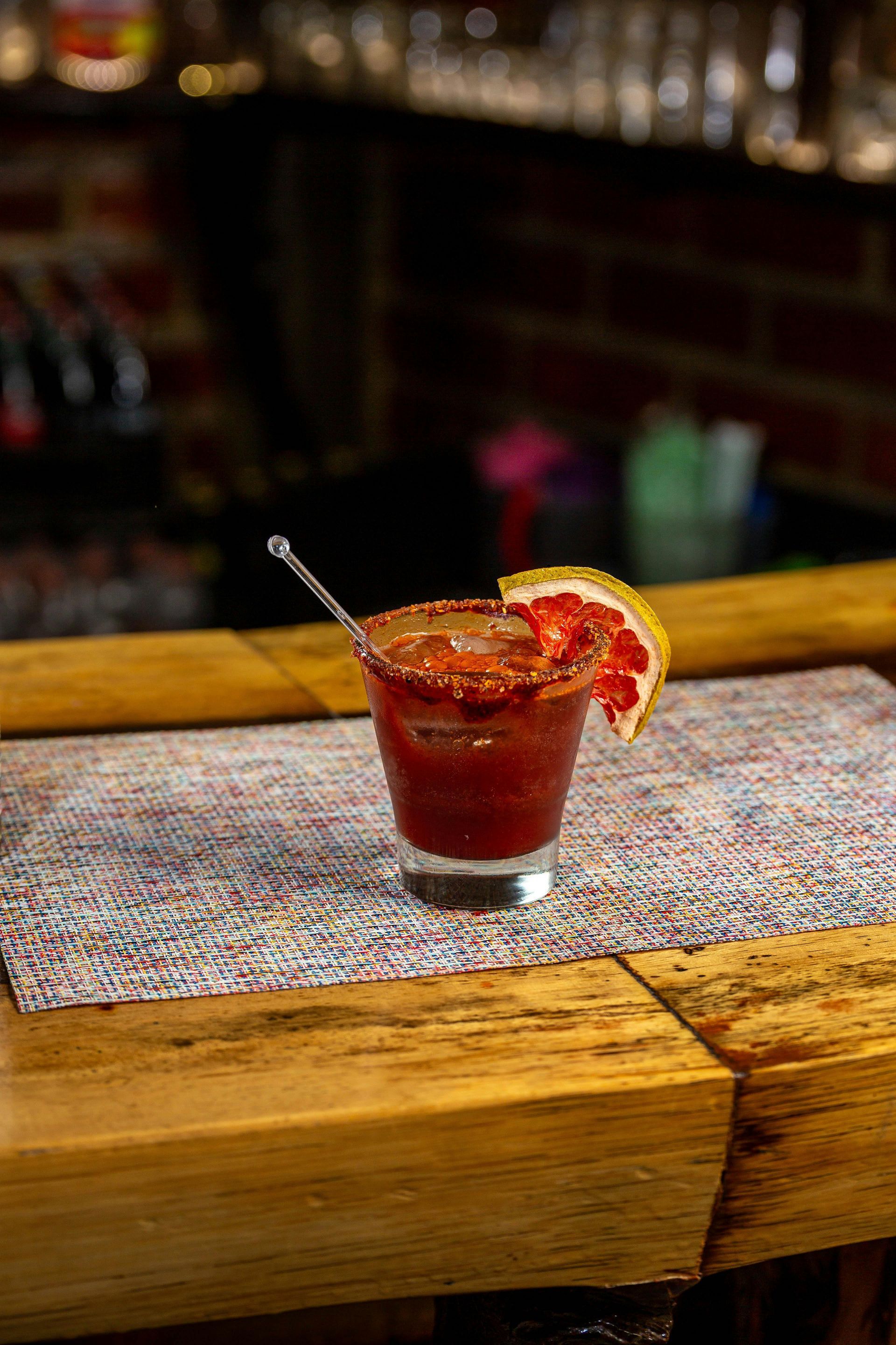 A red cocktail in a glass with a citrus garnish on a bar counter