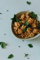 Bowl of seasoned rice or grain topped with green herbs on a white table