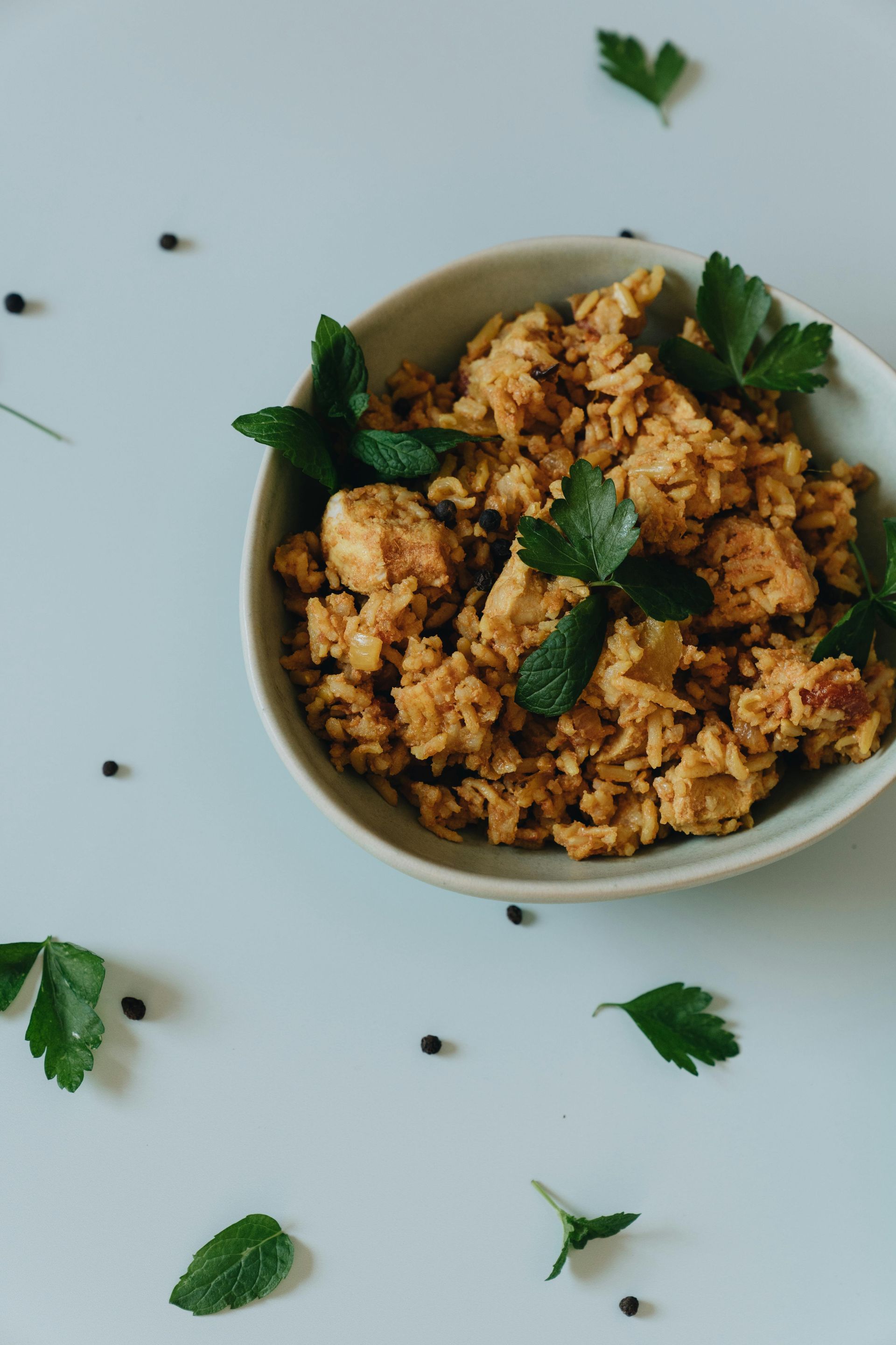 Bowl of seasoned rice or grain topped with green herbs on a white table