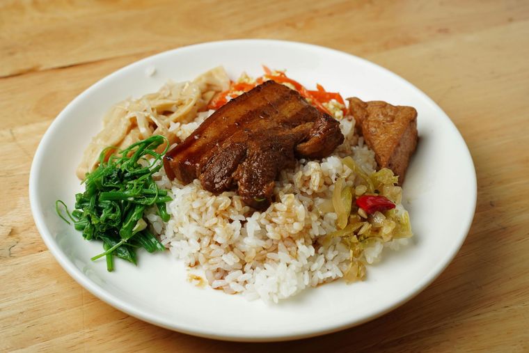 Plate of rice with braised meat, vegetables, and greens on a wooden table