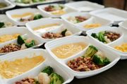 Meal-prep trays with vegetables, beans, and yellow sauce arranged in rows on a table