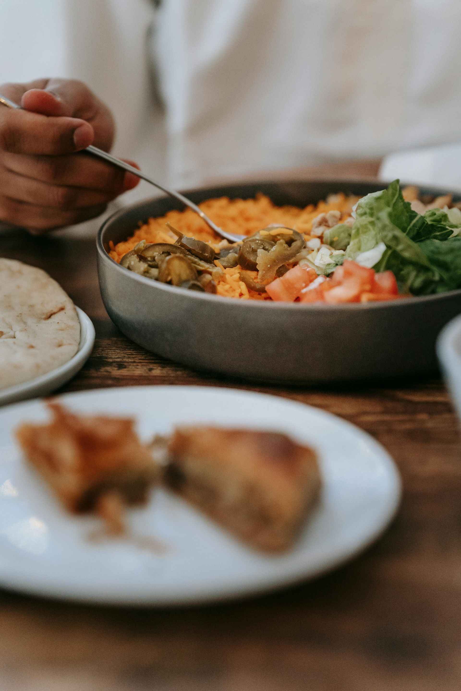 Person eating a rice bowl with greens and salmon at a table, with bread and a fork nearby