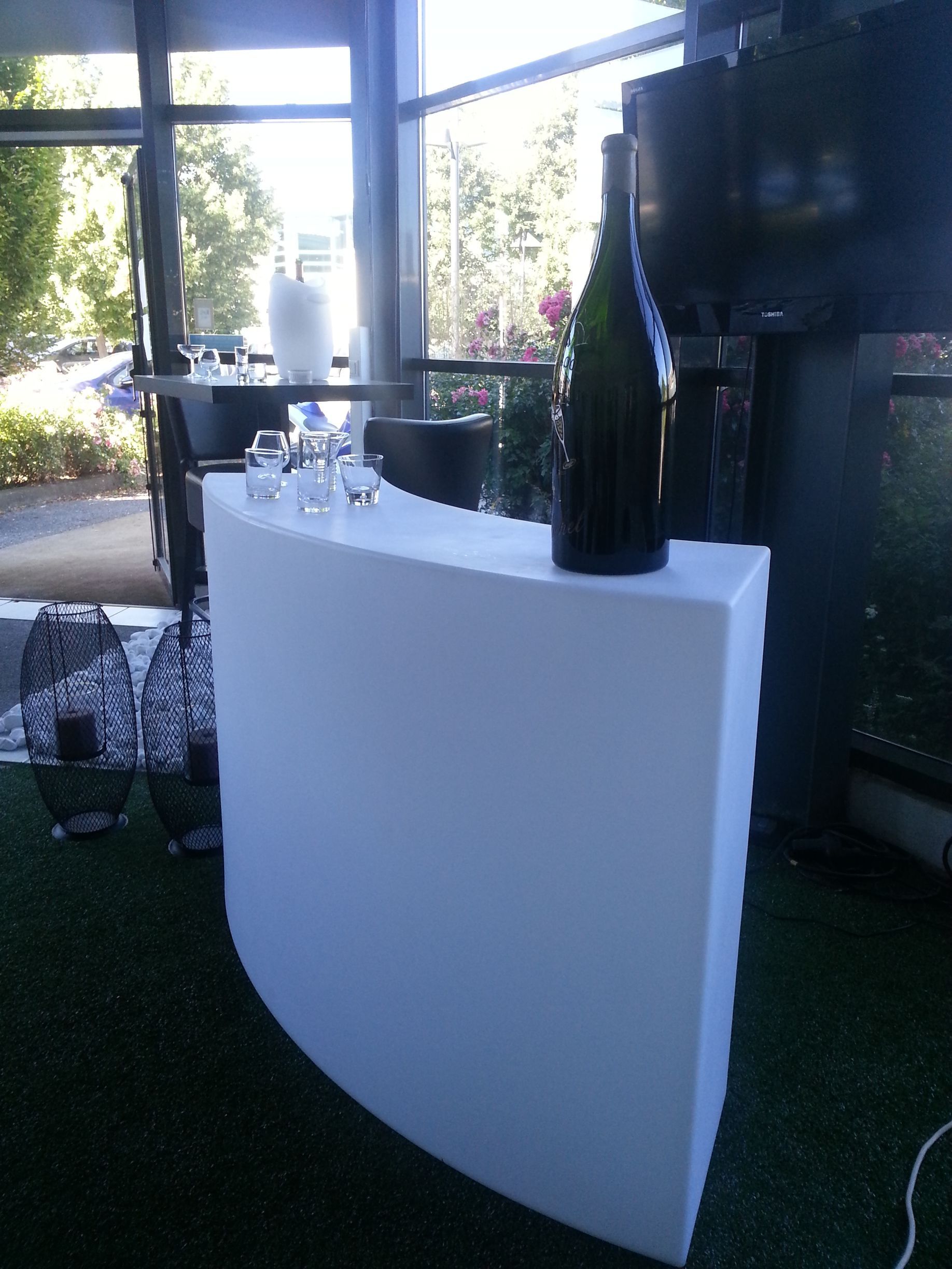 Table de bar blanche incurvée avec bouteille de vin et verres dans un cadre extérieur ensoleillé