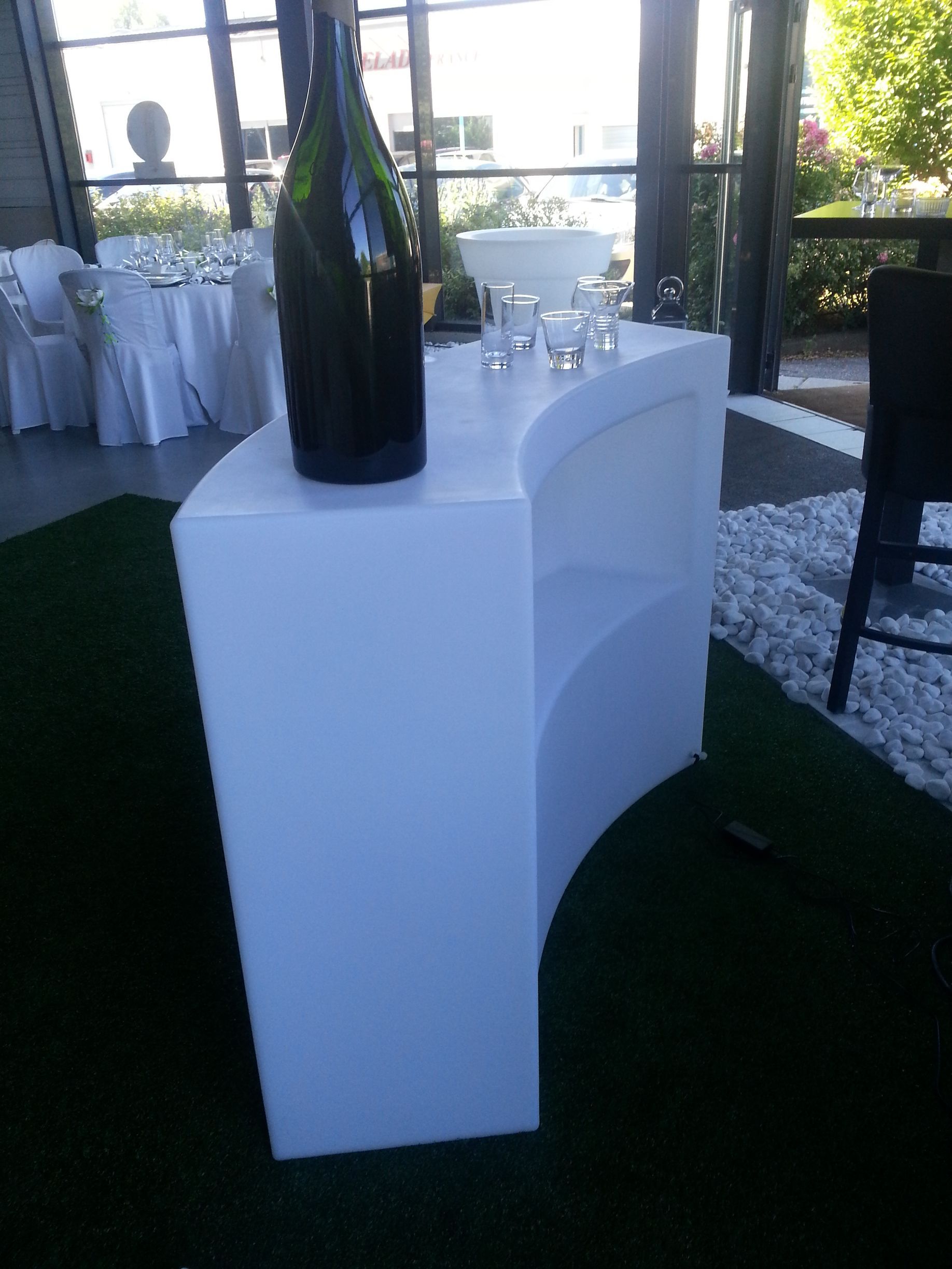 Table de bar blanche incurvée avec bouteille de vin et verres dans un cadre extérieur ensoleillé