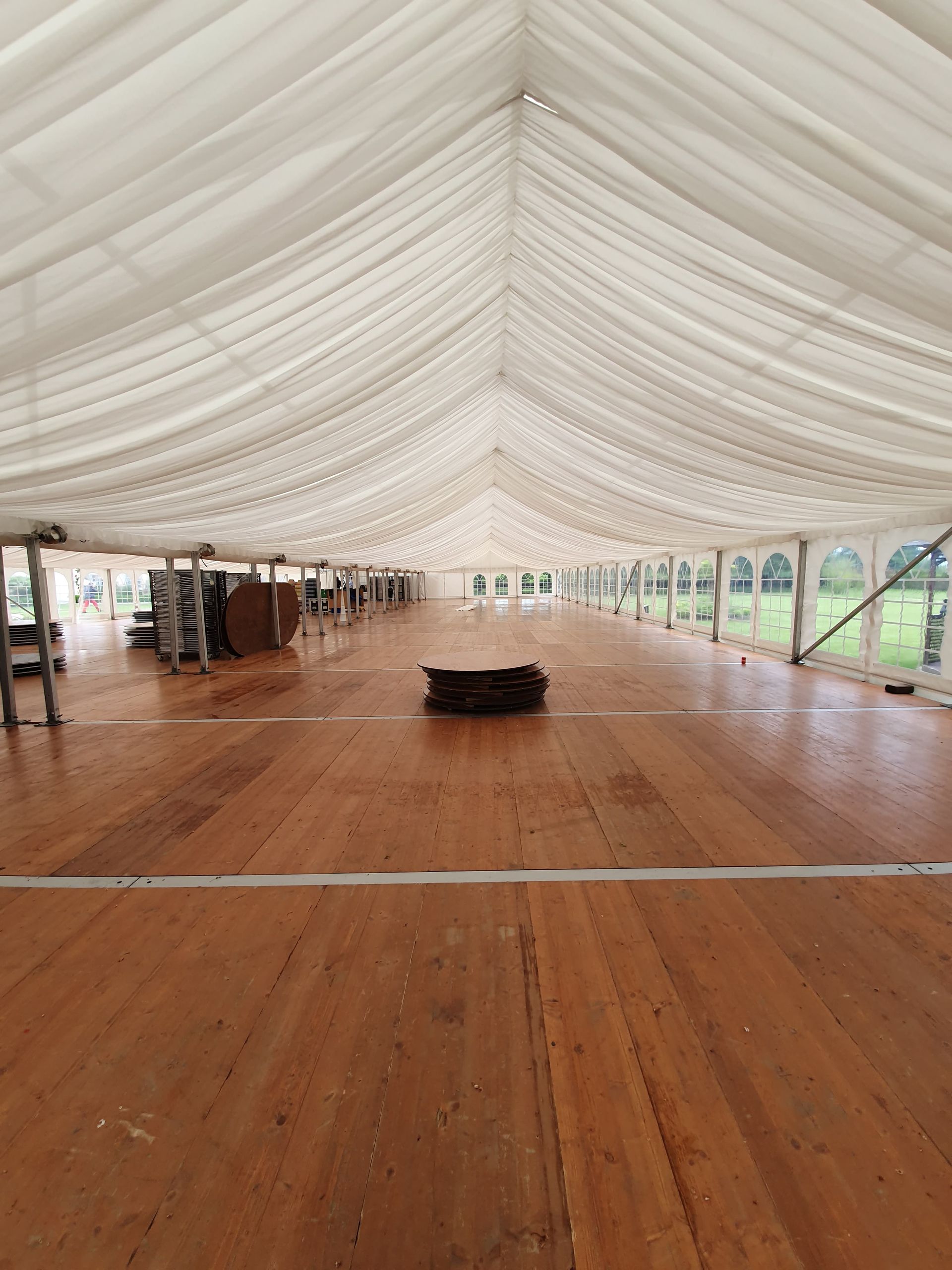 Grande tente blanche vide avec un plancher en bois et un petit tabouret noir au centre