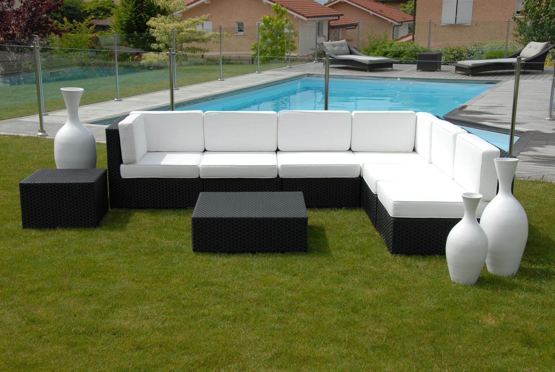 Canapé d'angle blanc d'extérieur avec tables noires sur une pelouse près d'une piscine