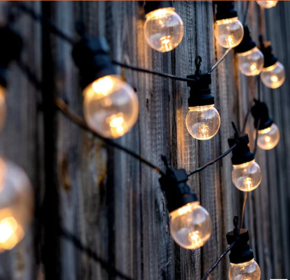 Des guirlandes lumineuses aux tons chauds illuminent un mur extérieur sombre au crépuscule.