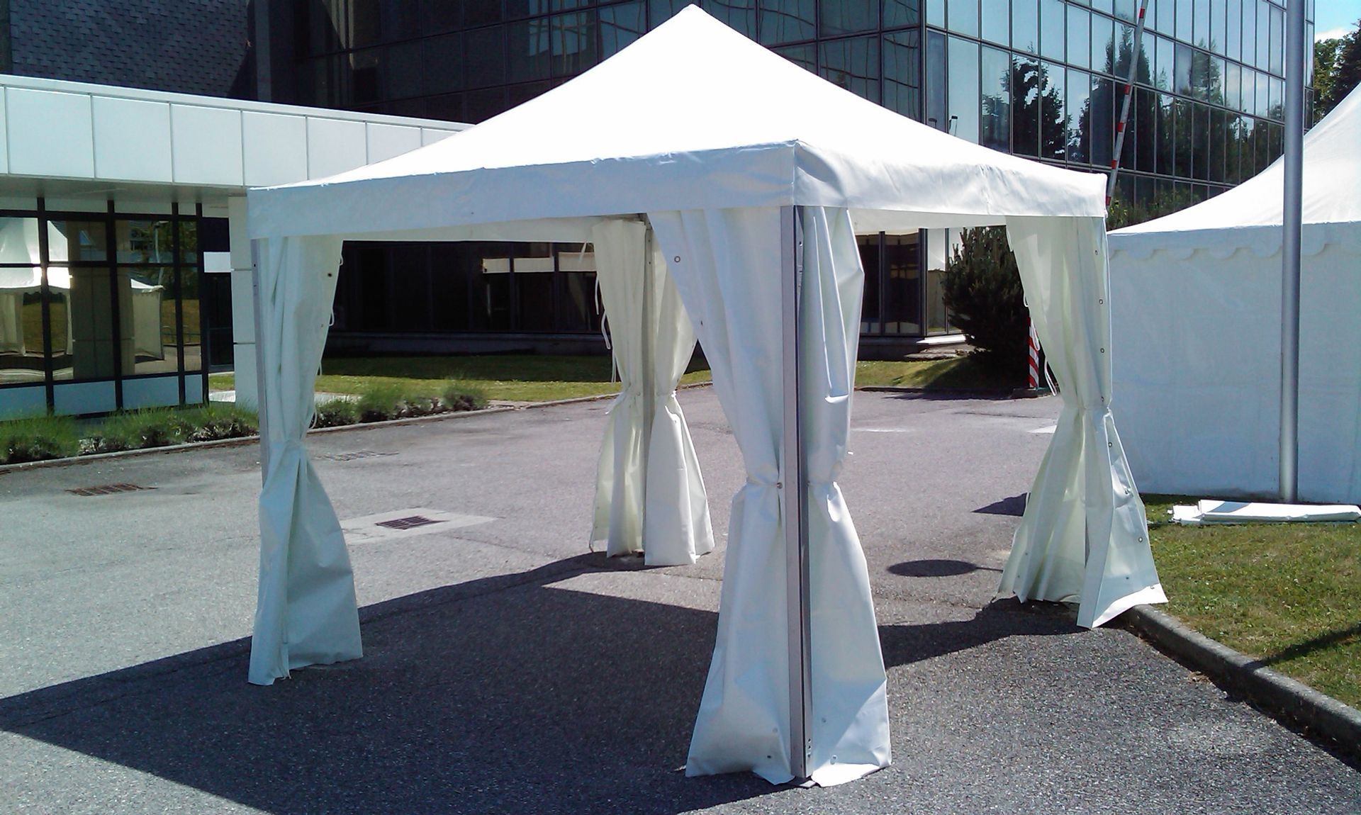 Tente pliante blanche installée sur le trottoir devant un bâtiment vitré