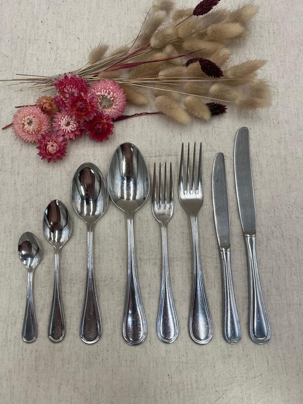 Assortiment de couverts comprenant cuillères, fourchettes, couteaux et fleurs séchées sur une surface claire