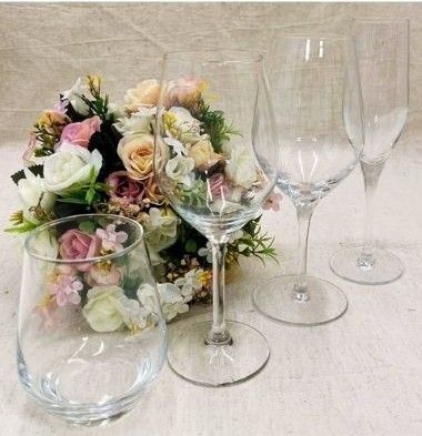 Des verres à vin transparents à côté d'un bouquet de fleurs pastel sur une nappe blanche