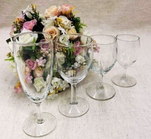 Quatre verres à vin transparents ornés d'un bouquet de fleurs pastel sur fond de tissu clair.