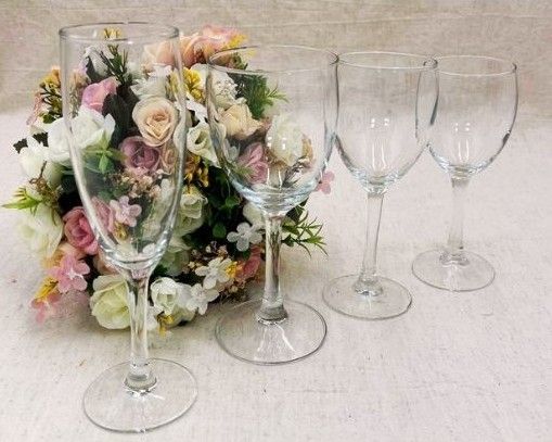 Quatre verres à vin vides à côté d'un arrangement floral pastel sur une nappe blanche.