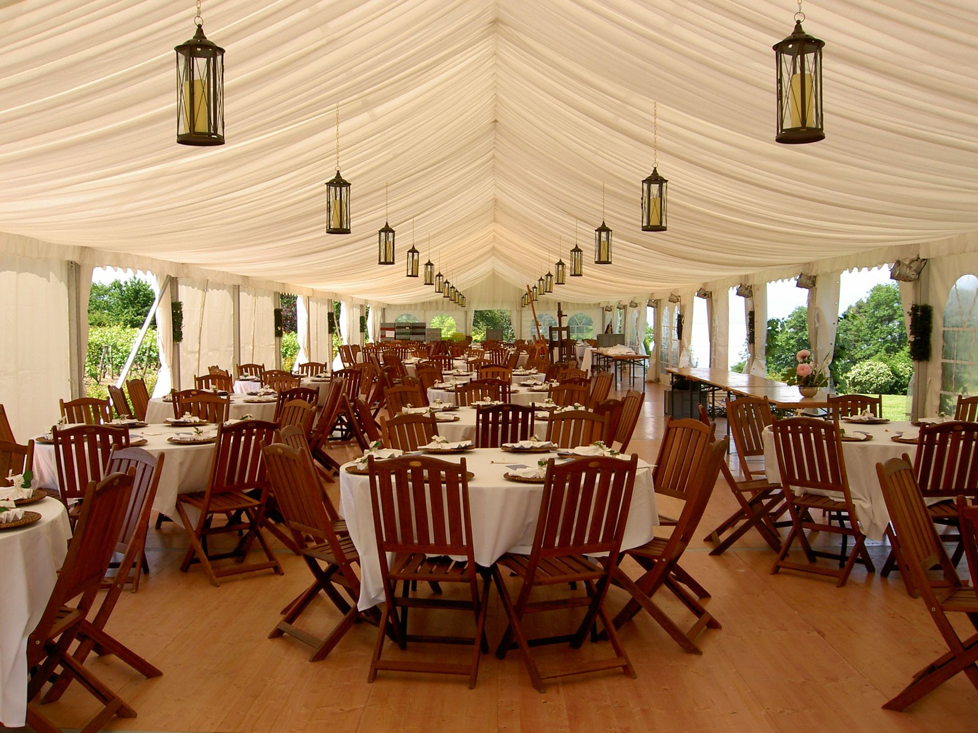 Élégante tente blanche pour réception de mariage, avec plafond drapé, lustres et tables décorées de fleurs
