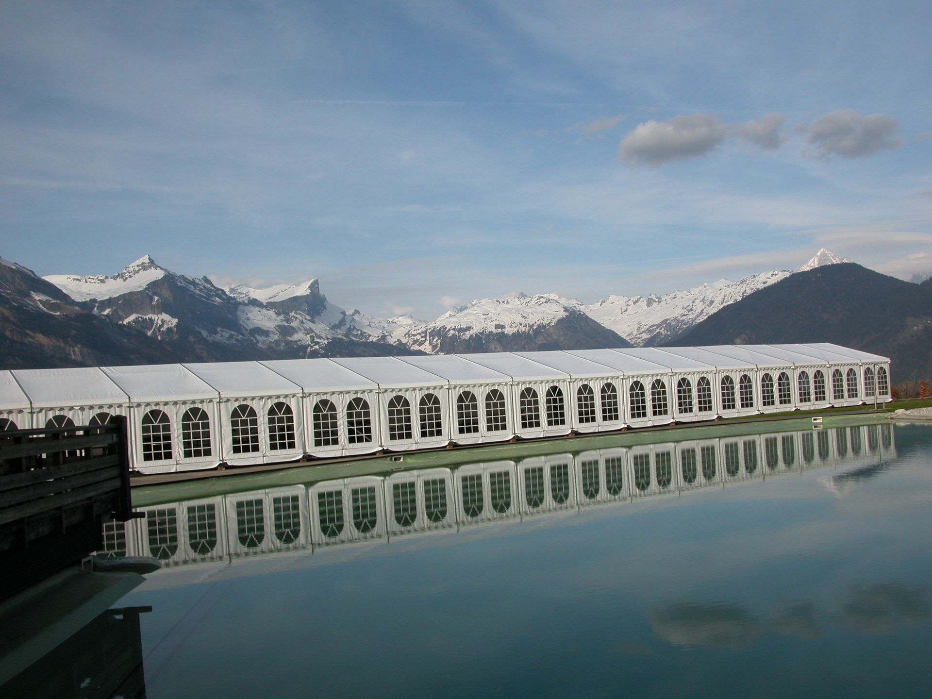 Lac de montagne enneigé avec un long bâtiment blanc en forme d'arche se reflétant dans l'eau calme