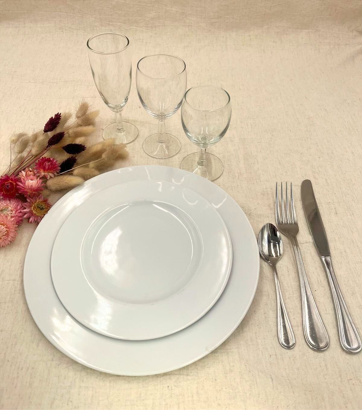 Élégante table dressée avec assiettes blanches, verres, couverts et composition florale sur une nappe beige