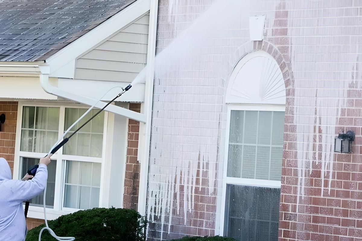 A Melo Powerwashing & Painting employee is cleaning the side of a brick house with a high pressure washer in ocean city, nj