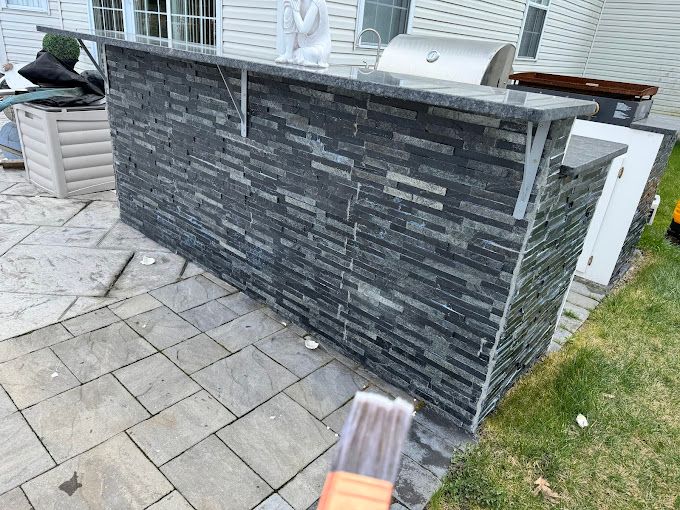 Outdoor bar with dark stacked stone facing, granite countertop, and stainless steel supports repaired by melo powerwashing & panting in linwood, nj