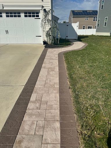Newly installed stone pathway leads from a driveway, framed by brown borders, through a grassy yard installed by melo powerwashing & painting in linwood, nj