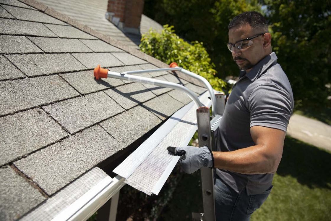 A man is standing on a ladder fixing a gutter on a roof