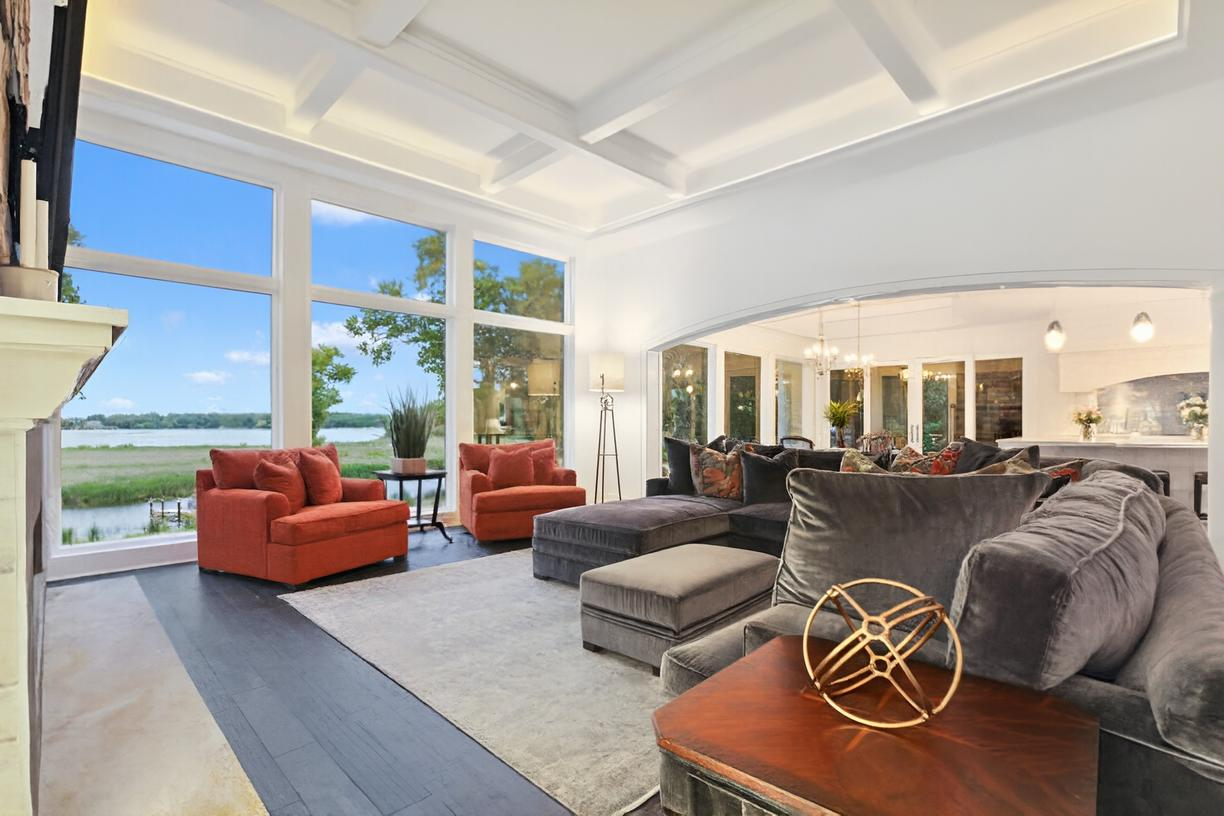 Bright modern living room with red chairs, gray sofas, and large windows overlooking the water