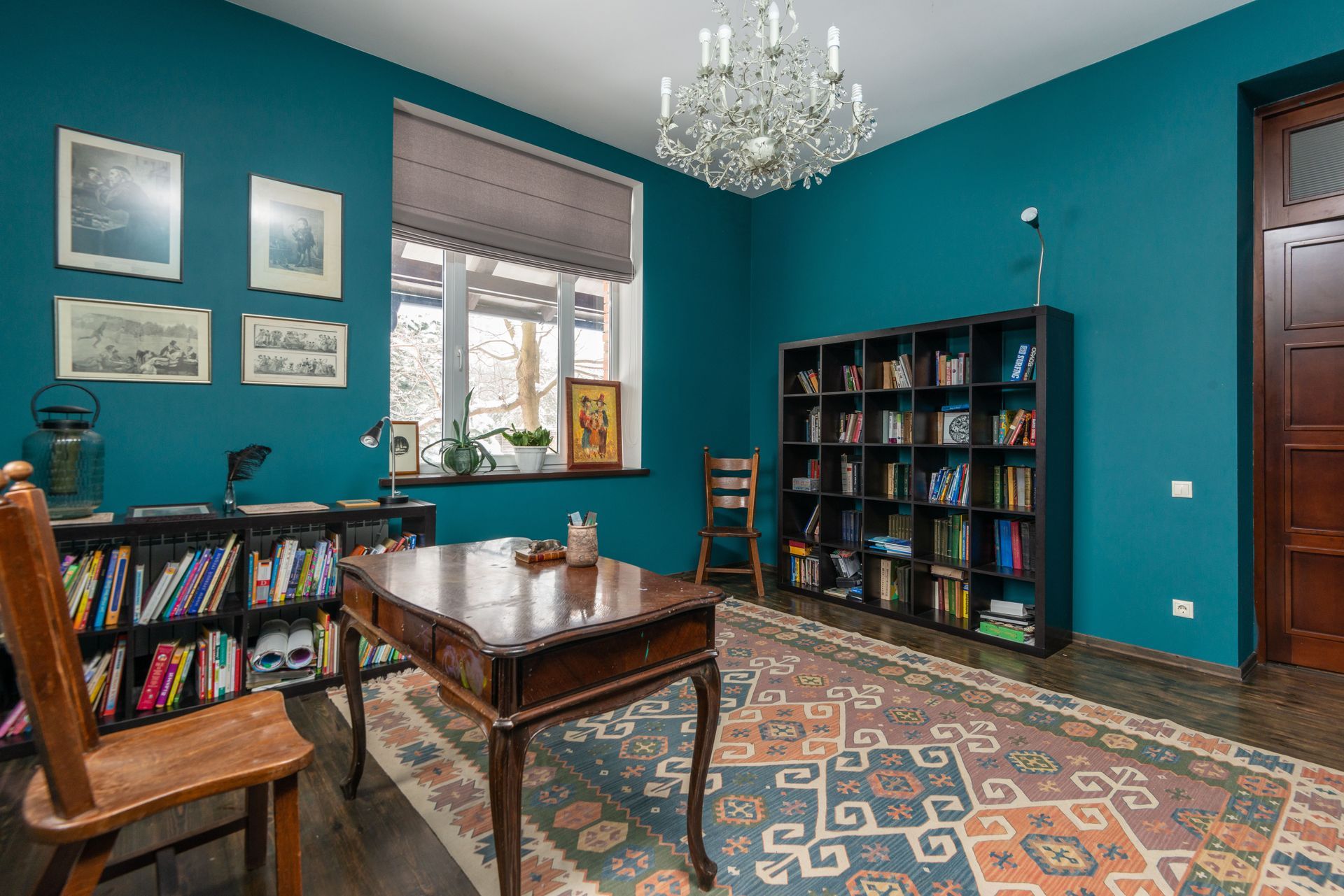 Teal home office with bookshelves, desk, window, rug, and chandelier