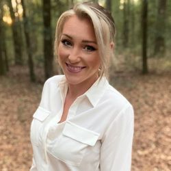 A woman in a white shirt is smiling in the woods.