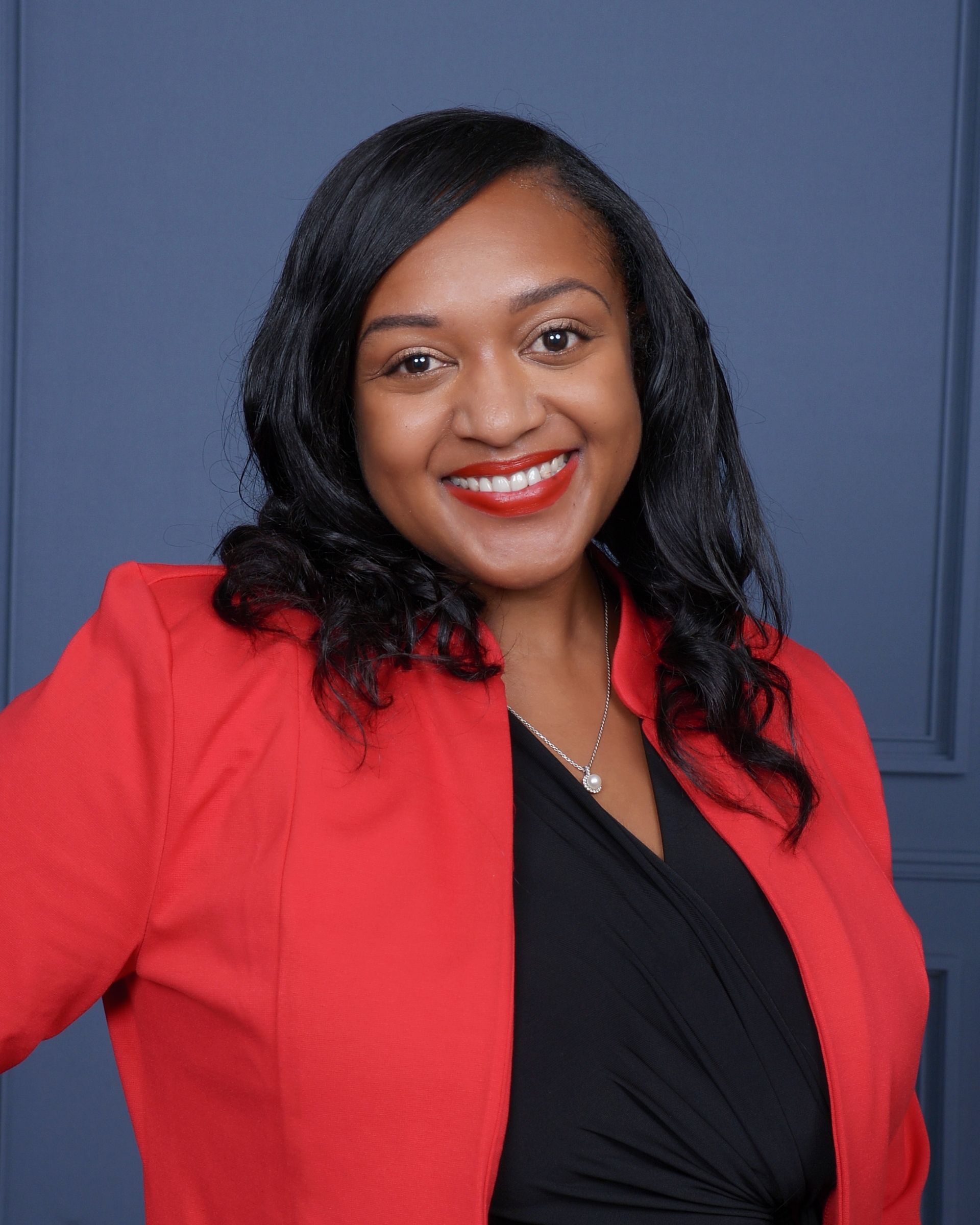 A woman in a red jacket and black dress is smiling for the camera.