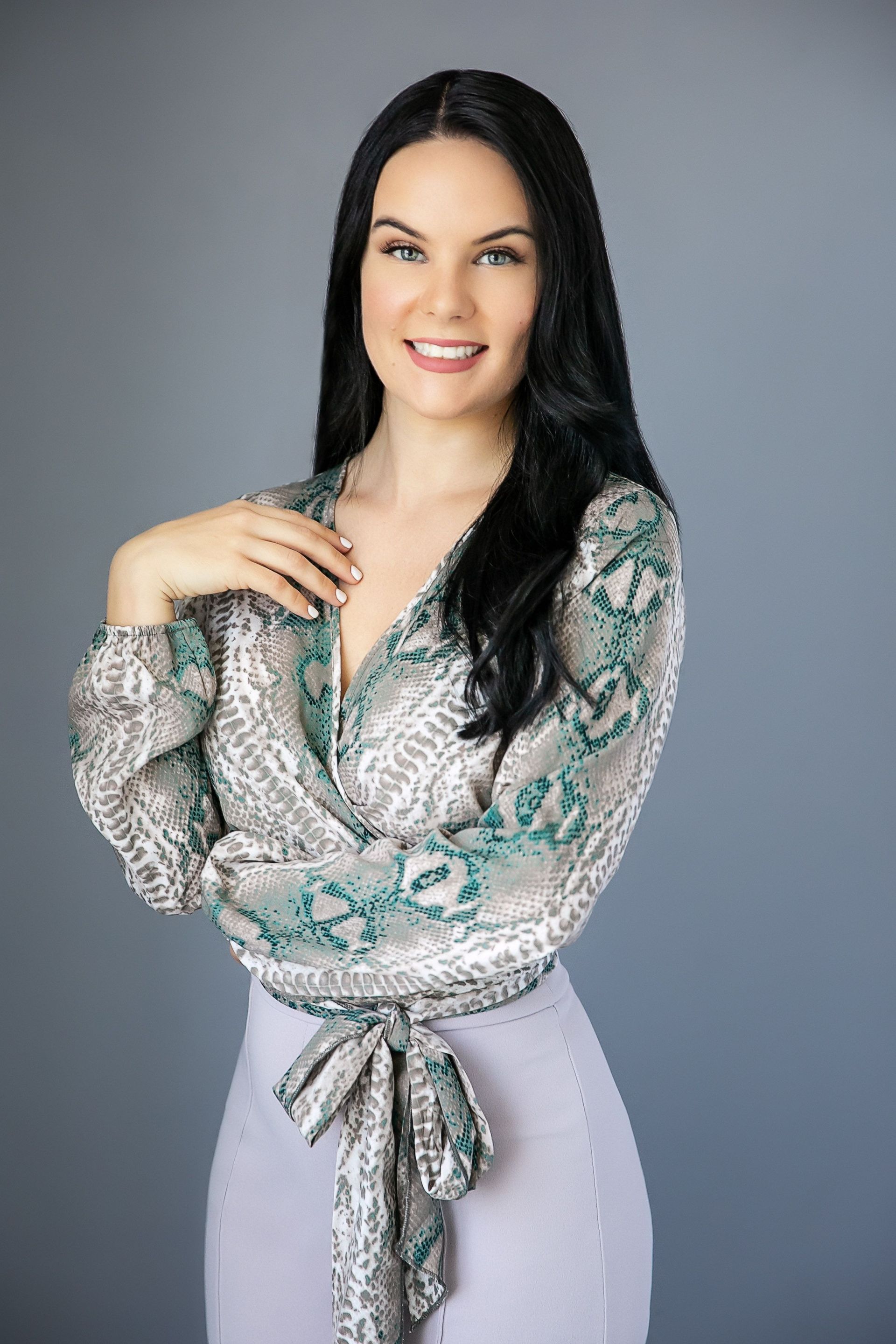 A woman is wearing a snake print wrap top and white pants.