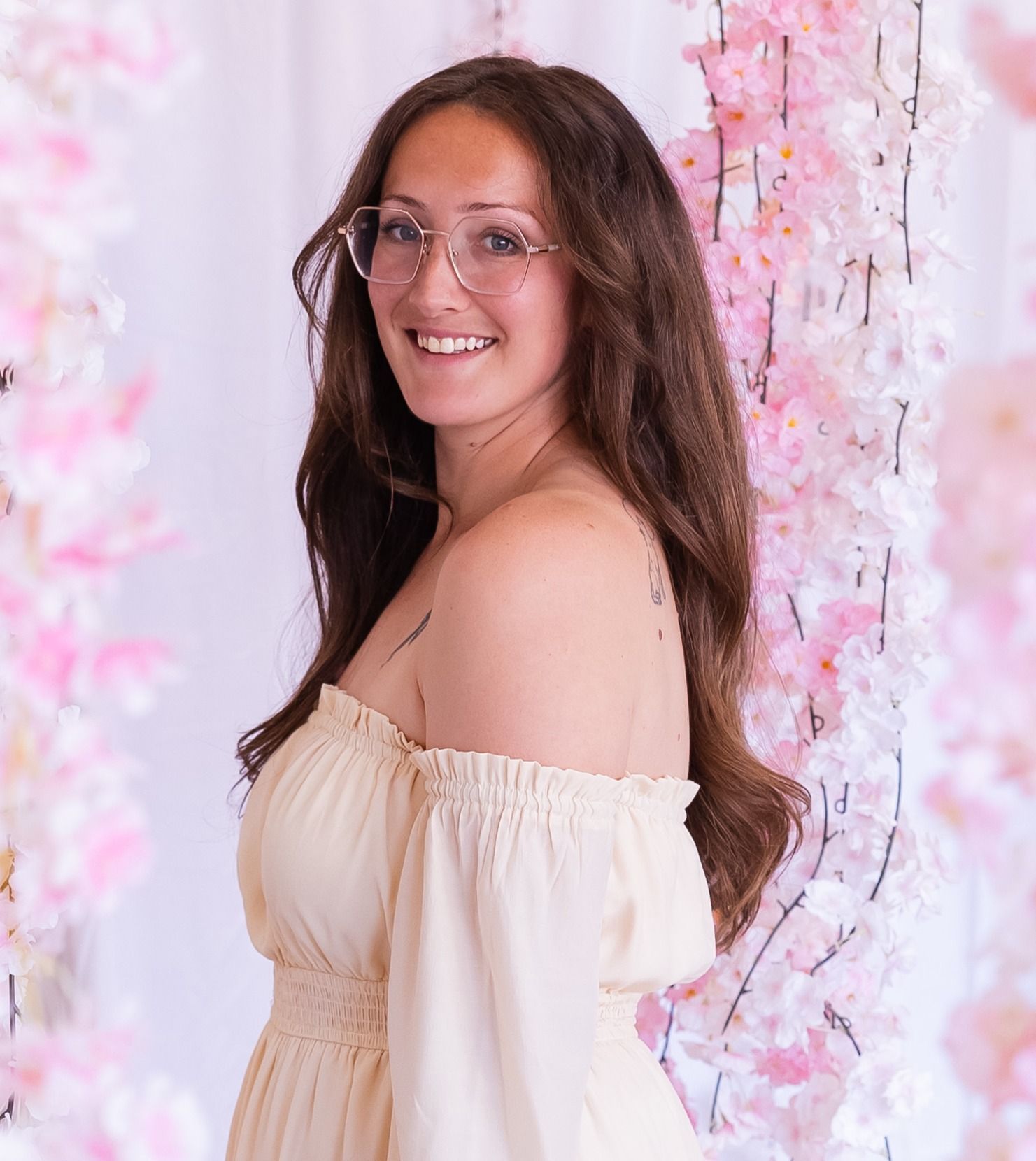 A woman wearing glasses and a necklace is standing in front of a window in a living room.