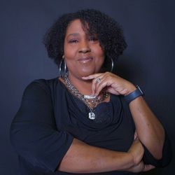 A woman wearing a black shirt and a necklace is standing with her arms crossed.