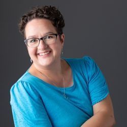 A woman wearing glasses and a blue shirt is smiling for the camera.