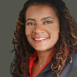 A woman with curly hair and dreadlocks is smiling for the camera.